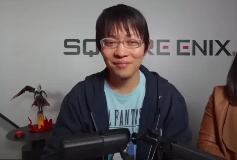 Naoki Hamaguchi يرتدي نظارات وقميصاً أزرق، ويجلس أمام جدار عليه شعار Square Enix.