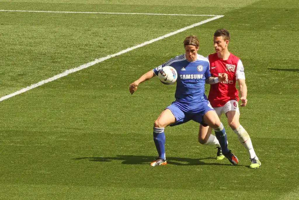Fernando Torres يرتدي طقم Chelsea الأزرق ويسيطر على كرة القدم بينما يظهر Laurent Koscielny خلفه.